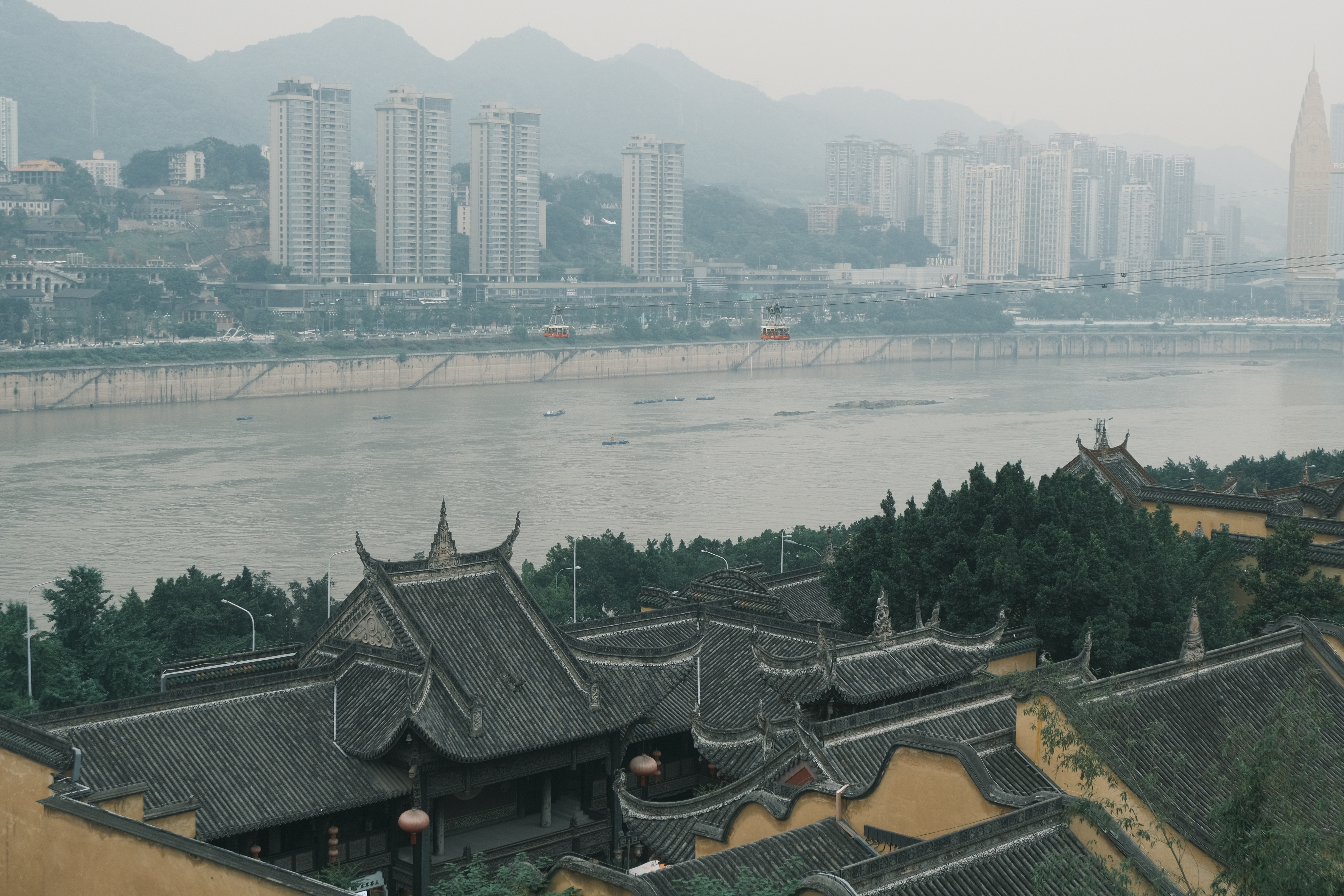 A misty riverside cityscape seen above traditional rooftops